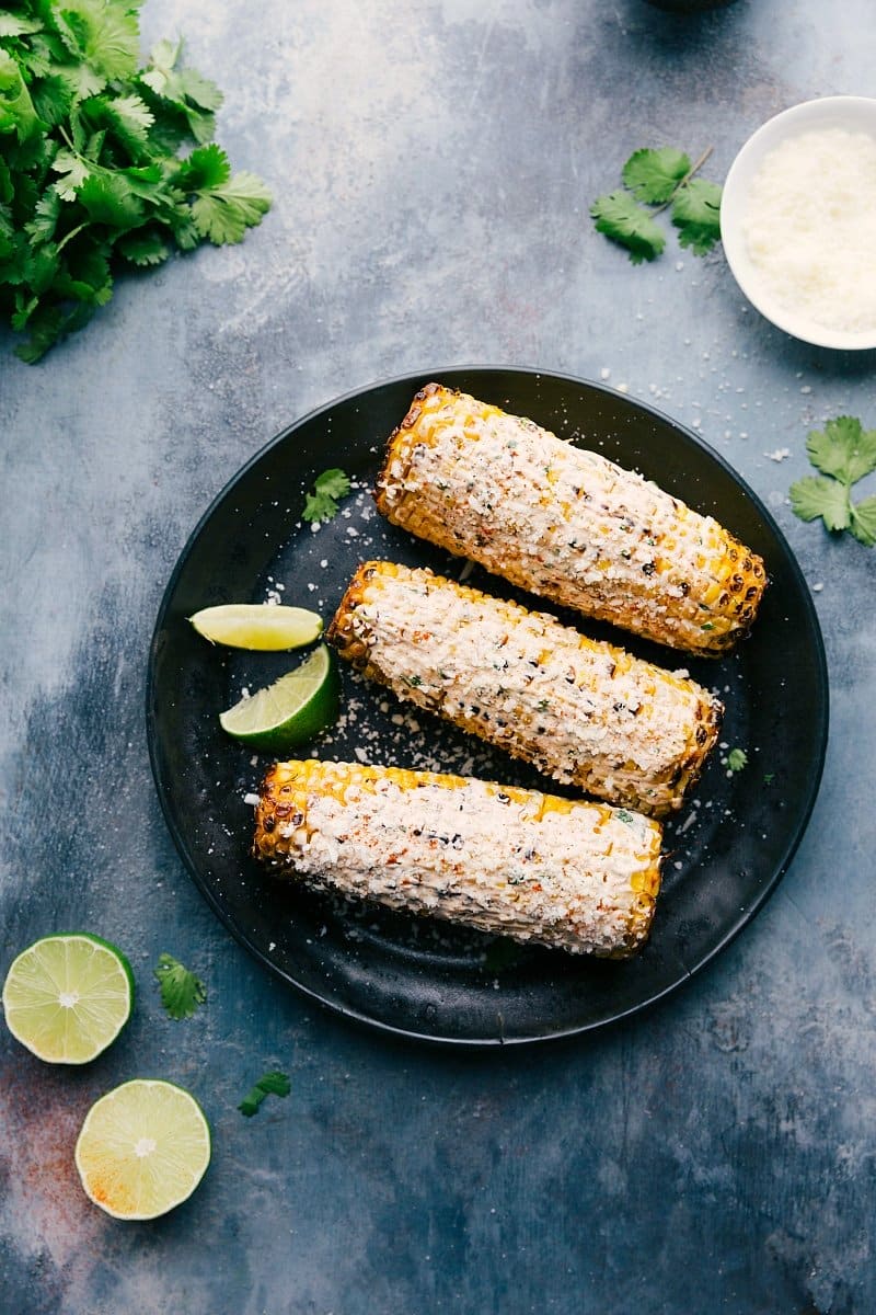 Elote with Limes and Cilantro Ready-to-eat elote on a plate with limes and cilantro around them, roasted and seasoned to perfection.