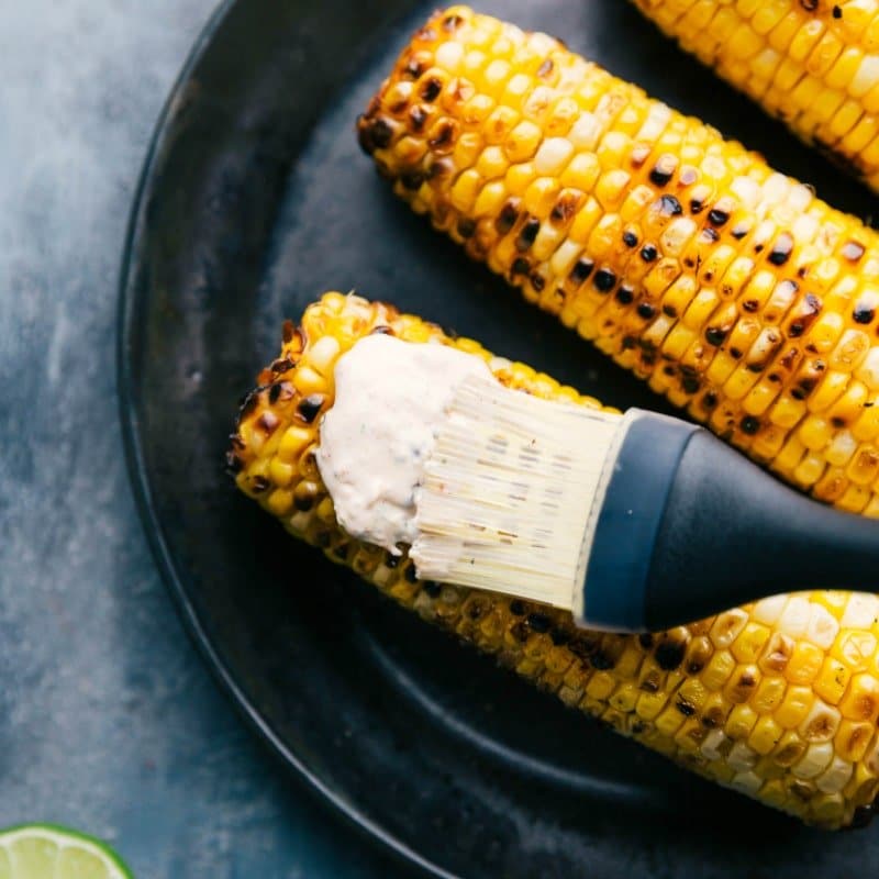 Spreading Cream Sauce on Roasted Corn Cream sauce being spread on roasted corn with a pastry brush for the elote recipe.