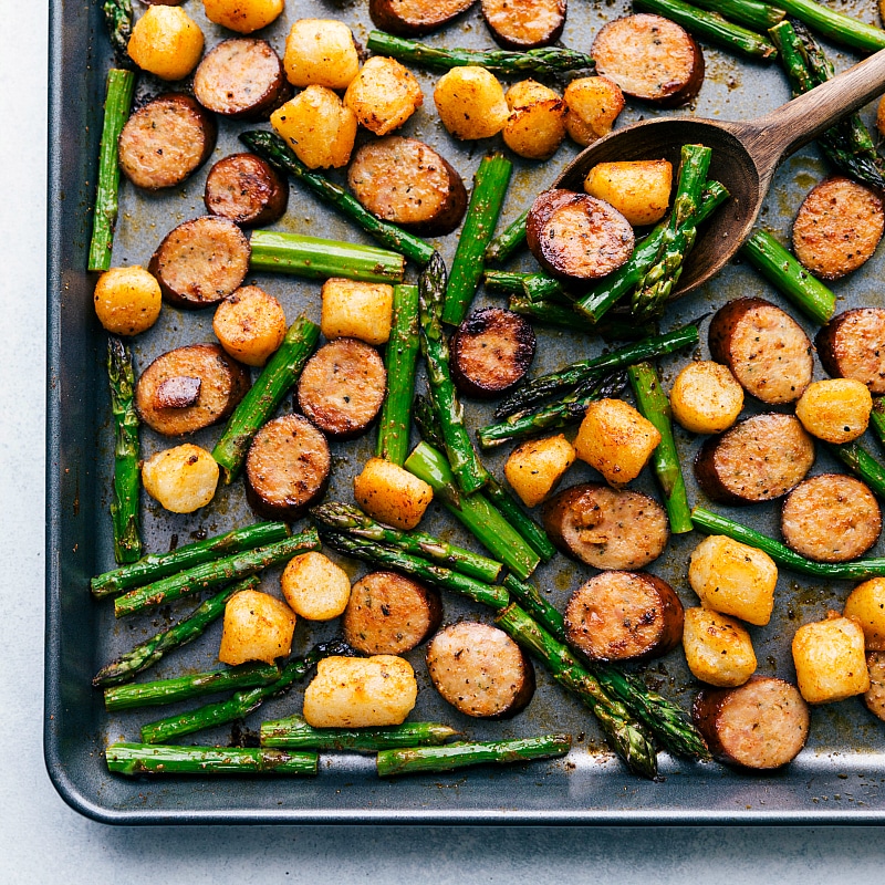 One pan and only EIGHT amazing ingredients make this flavor-packed and nutritious Sausage Pesto and Veggies!ย chelseasmessyapron.com #one #pan #easy #recipe #sausage #pesto #asparagus #chicken #sundried #tomatoes Process shot of meal: sausage, asparagus, and gnocchi roasting.