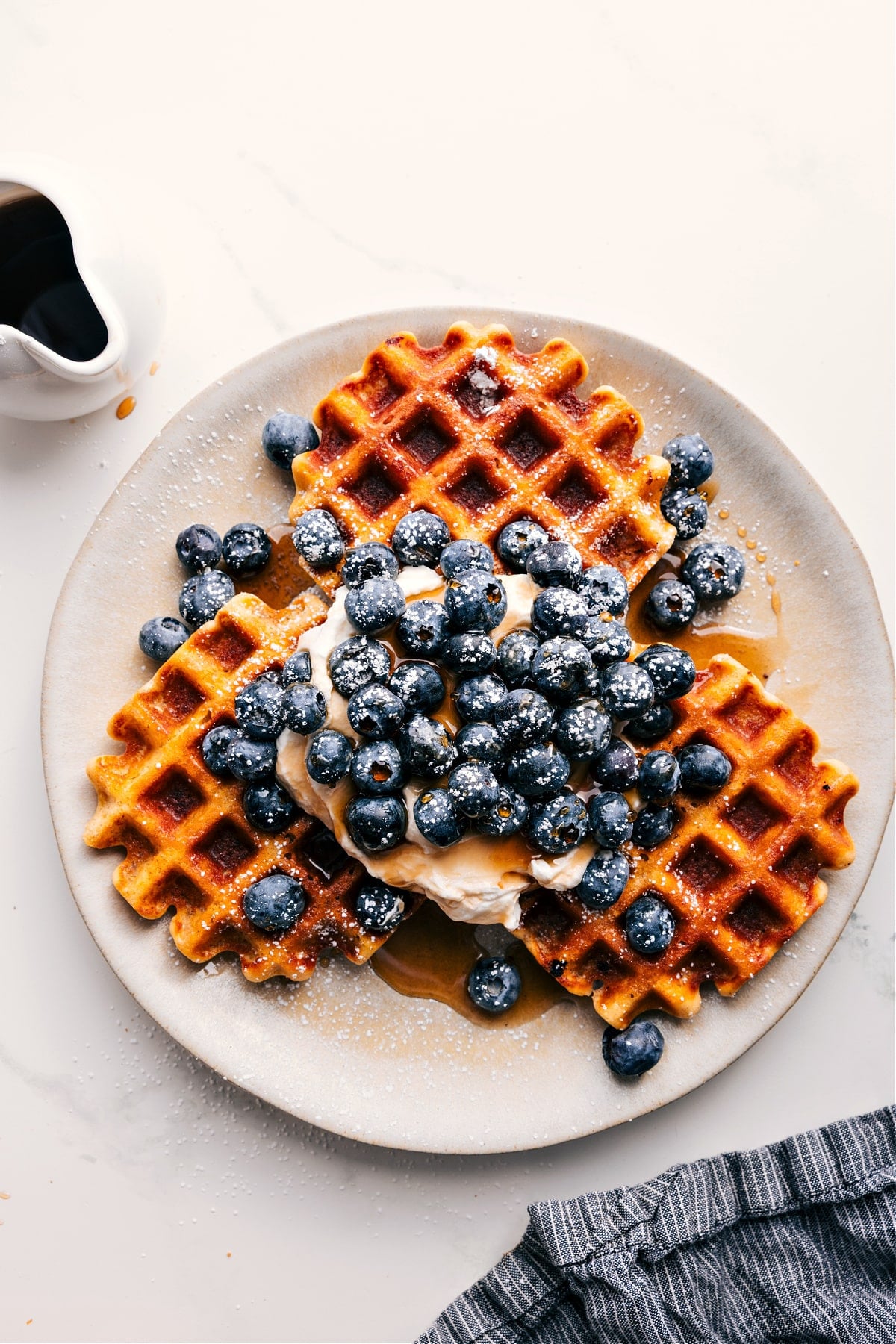 Waffle recipe served on a plate with whipped cream, blueberries, and maple syrup.