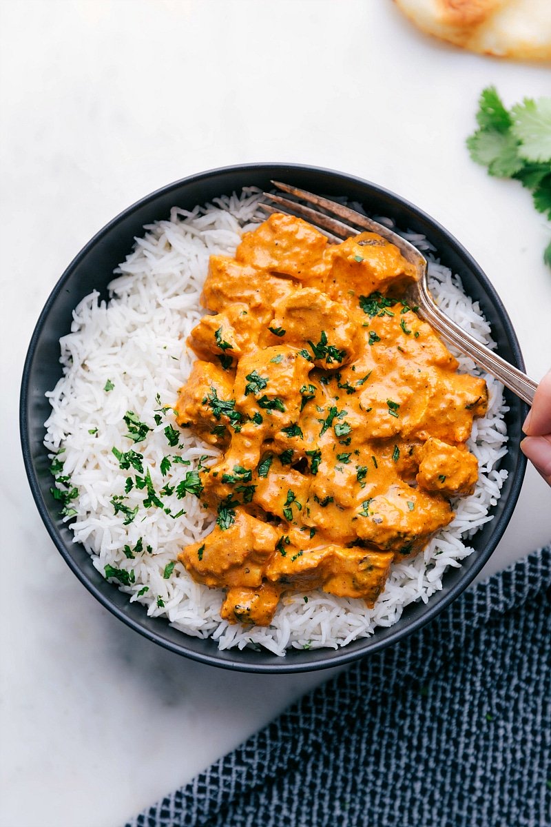 Chicken Tikka Masala with Rice Bowl of chicken tikka masala served with rice, with a fork digging in, showcasing tender chicken pieces in a creamy, spiced sauce.