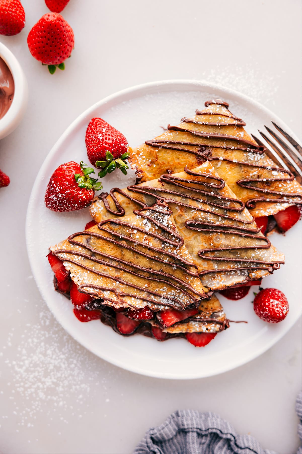 Finished Nutella crepes, generously filled with strawberries and cream, with a rich Nutella drizzle on top and a dusting of powdered sugar.