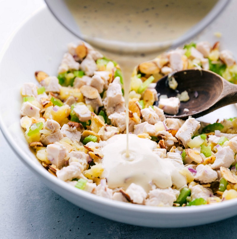 Dressing being poured over the chicken salad with pineapple, ready to be mixed for a delicious meal.