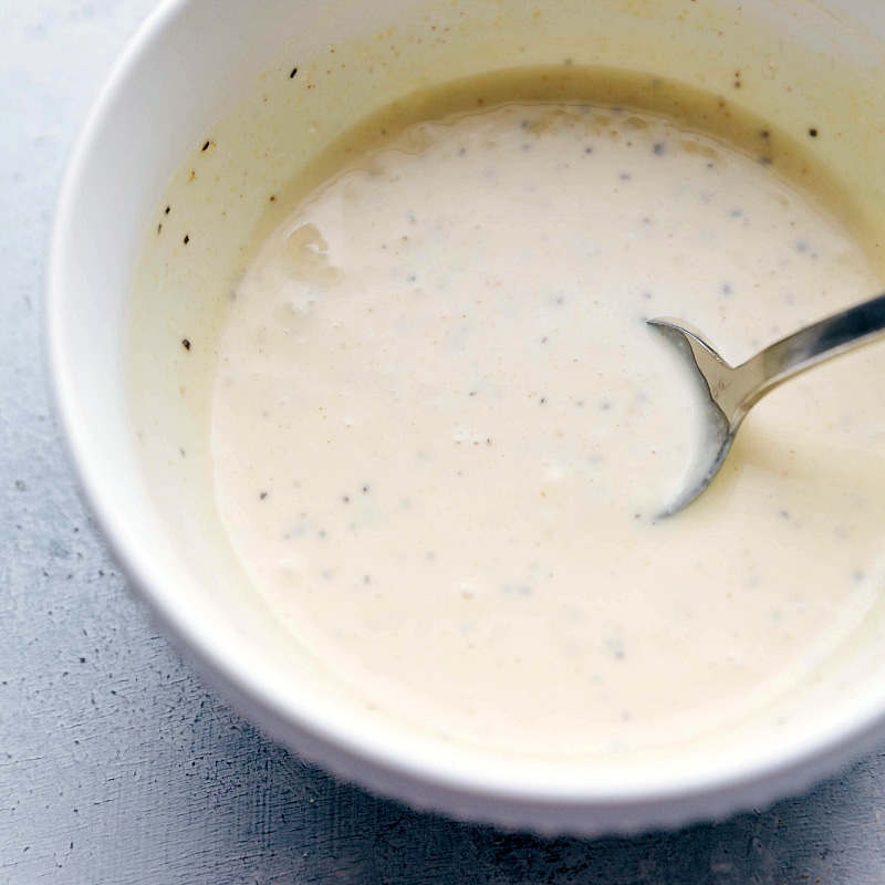 Dressing ingredients being mixed together in a small bowl, combining flavors for a smooth and flavorful sauce.