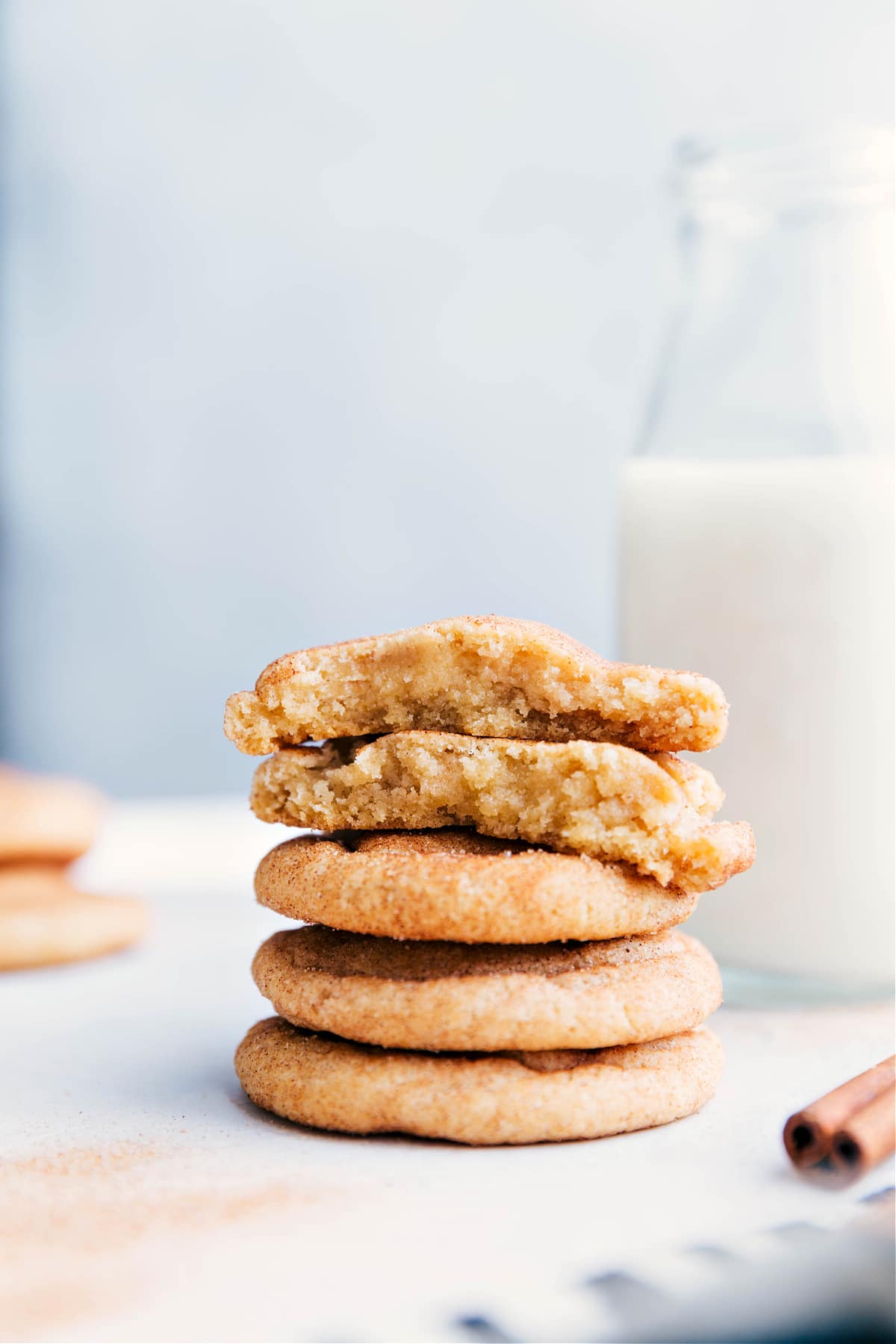Stack of freshly baked snickerdoodle cookies on a plate, with one broken in half to reveal the soft and delicious interior.