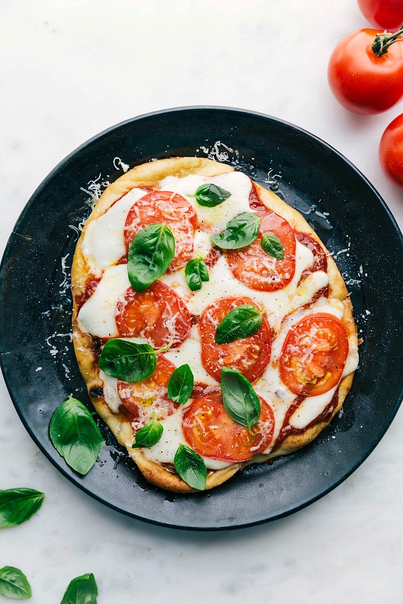 A delicious baked naan pizza on a plate, topped with fresh basil leaves, melted cheese, and vibrant toppings.