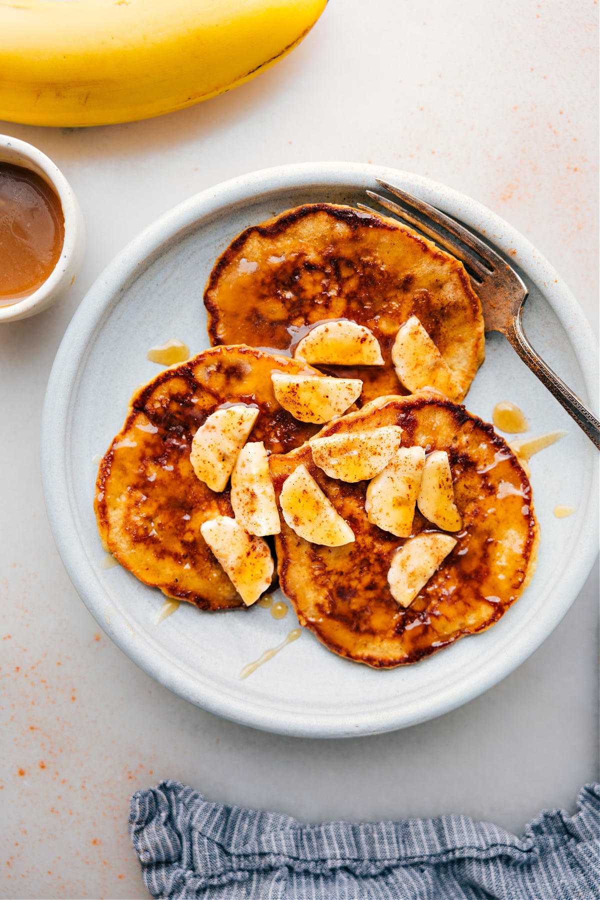 Warm banana pancakes stacked on a plate, topped with fresh banana slices and generously drizzled with syrup, creating a delicious and inviting breakfast.