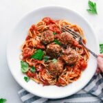 A bowl of finished turkey meatballs nestled over a bed of spaghetti, generously coated with marinara sauce and topped with fresh herbs, creating a hearty and inviting meal ready to be enjoyed.
