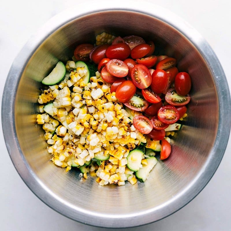 Corn and Zucchini Salad Ready for Mixing A bowl filled with the corn and zucchini salad, the addition of fresh tomatoes and more ingredients, capturing the moment before mixing to create a flavorful salad.