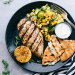 A plate featuring Greek chicken served with naan bread and a zucchini and corn salad, offering a delicious and flavor-packed meal.