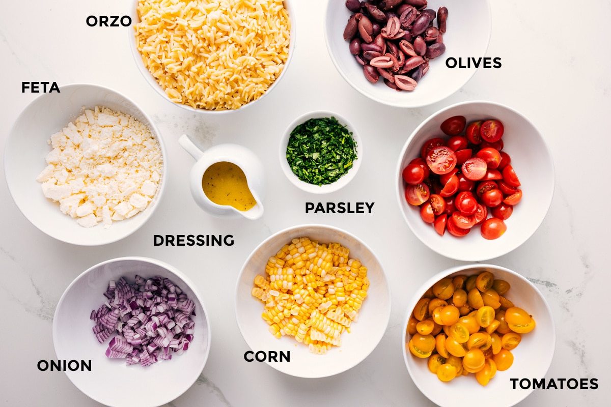 Ingredients In This Greek Orzo Pasta Salad All the ingredients in this recipe prepped out for easy assembly including the feta, onion, dressing, corn, tomatoes, olives, parsley, and orzo.