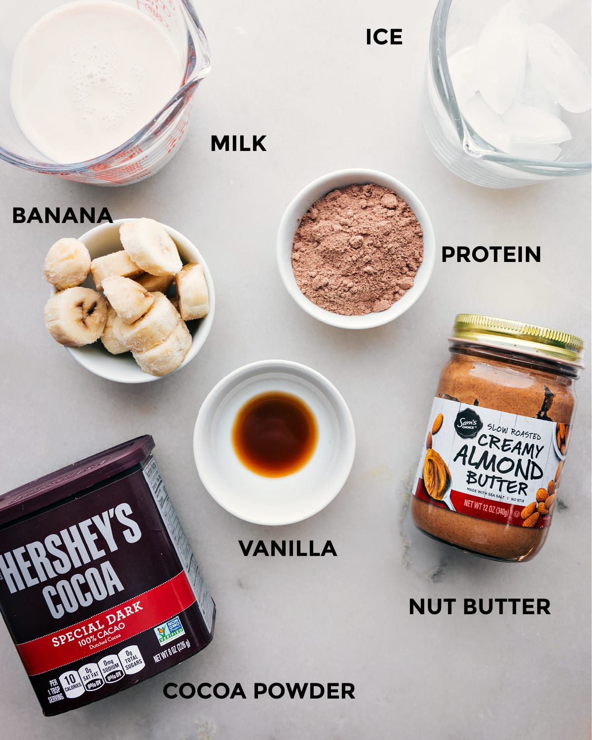 Ingredients In The Best Chocolate Protein Shake All the ingredients including milk, ice, cocoa powder, nut butter, vanilla, and protein powder prepped out for easy assembly.