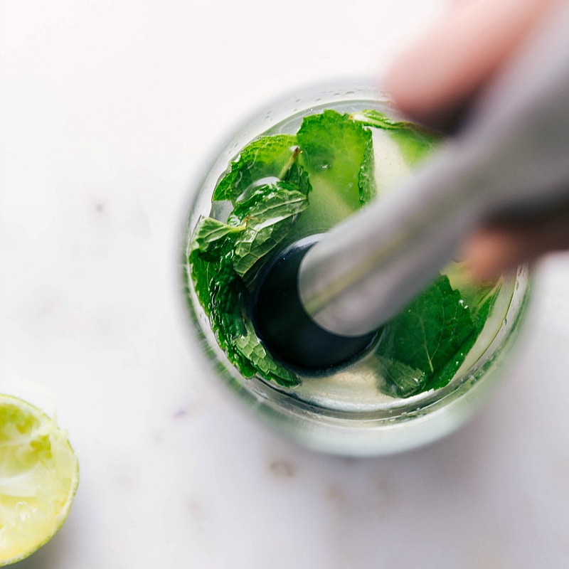 Mint leaves being muddled in a glass, releasing their aroma and flavor for the refreshing drink.