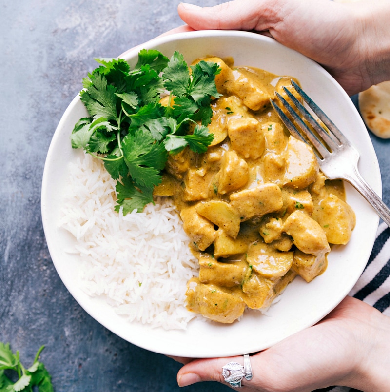 This authentic Thai Yellow Chicken Curry recipe with baby gold potatoes is comfort food at its finest! This easy to make curry can be ready in about 45 minutes or less. Recipe via chelseasmessyapron #thai #easy #recipe #Indian #healthy #coconutmilk #yellow #chicken #curry Finished meal on a bed of rice with fresh herbs on top, a hearty meal ready to be enjoyed.