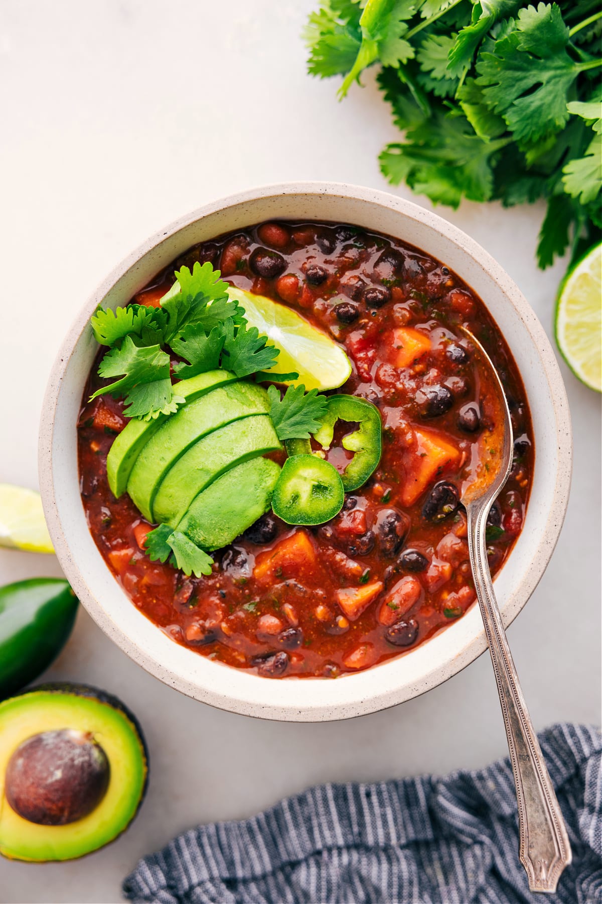 Sweet Potato Chili With All The Toppings Sweet Potato Chili served in a bowl, topped with cilantro, jalapeรฑo, lime, and avocado.
