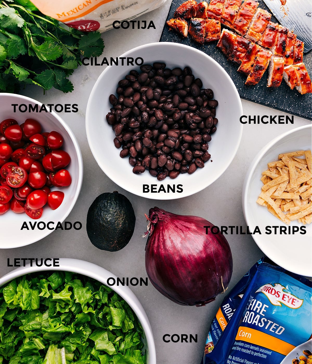 Ingredients Assmbled To Make This Delicious Dish. All the ingredients assembled, including cooked chicken, beans, tomatoes, cotija cheese, avocado, lettuce, onion, corn, and tortilla strips.