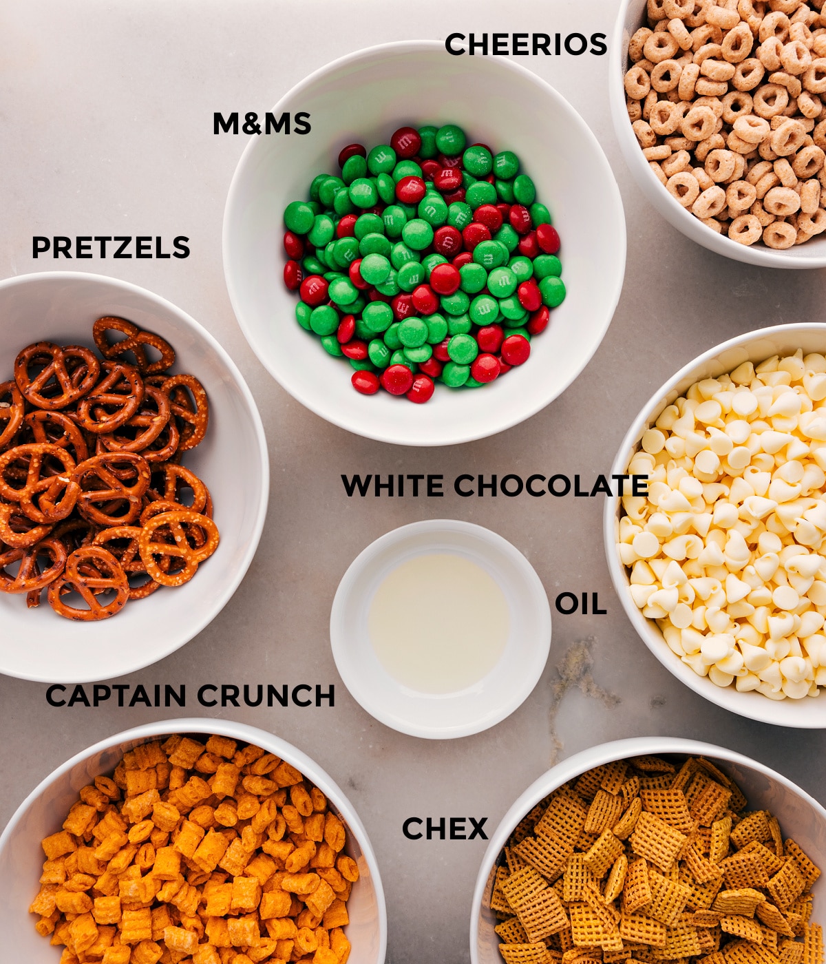 Ingredients In Christmas Snack Mix All the ingredients in this recipe are prepped for easy assembly: M&Ms, white chocolate, oil, Chex, Captain Crunch, and pretzels.