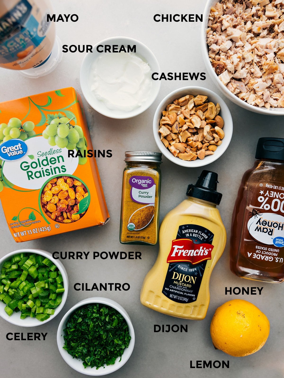 Ingredients In Curry Chicken Salad All the ingredients prepped out for easy assembly, including mayo, sour cream, chicken, cashews, raisins, cilantro, celery, dijon, honey, and lemon.