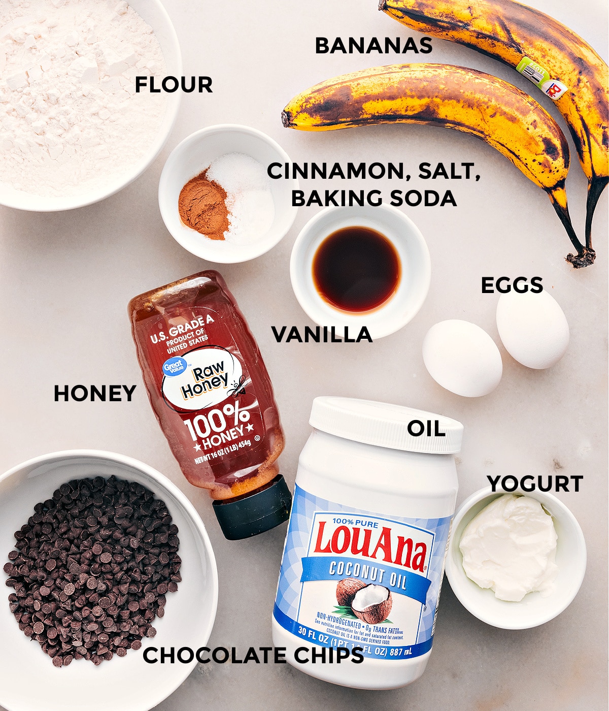 Ingredients In Healthy Banana Bread Recipe Ingredients in this recipe prepped out for easy assembly including flour, bananas, cinnamon, salt, baking soda, eggs, vanilla, honey, chocolate chips, oil, and yogurt.