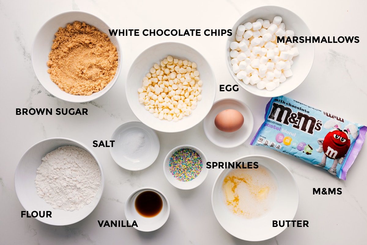 Ingredients In Confetti Bars All the ingredients in this recipe prepped out for easy assembly including the brown sugar, flour, vanilla, salt, white chocolate chips, marshmallows, egg, M&Ms, butter, and sprinkles.