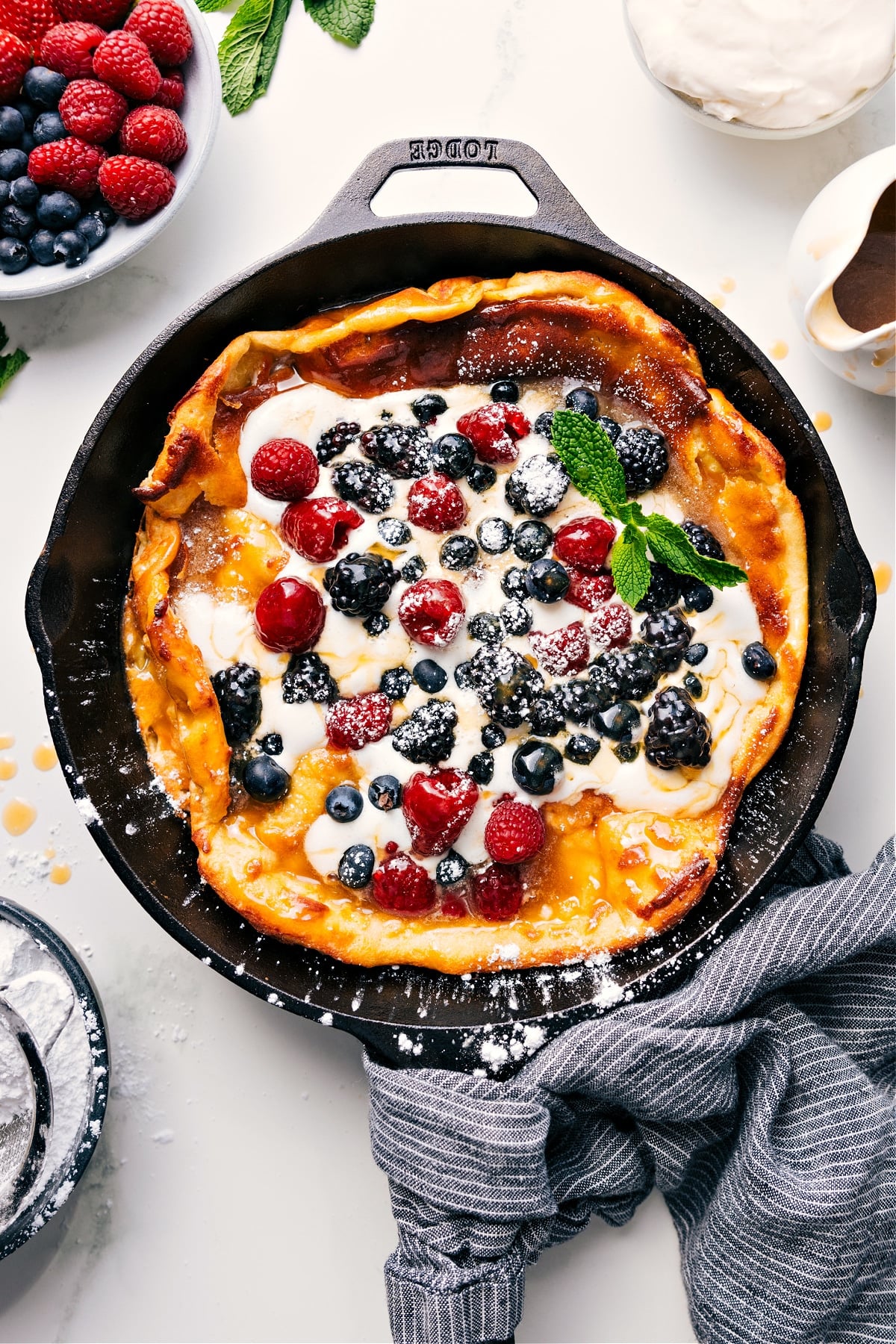 Dutch Baby skillet topped with fresh whipped cream, berries, and syrup.