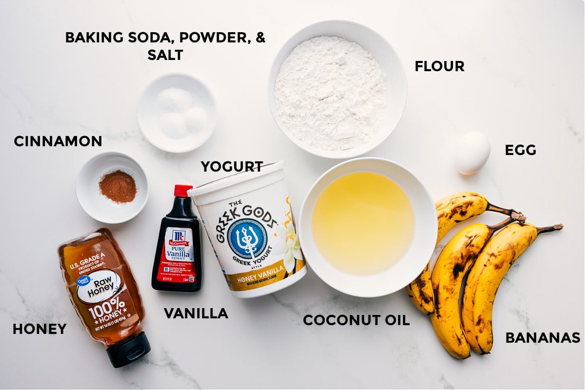 Ingredients In Healthy Banana Muffins All the ingredients prepped for easy assembly, including flour, eggs, fruit, coconut oil, yogurt, baking soda, powder, salt, cinnamon, vanilla, and honey.