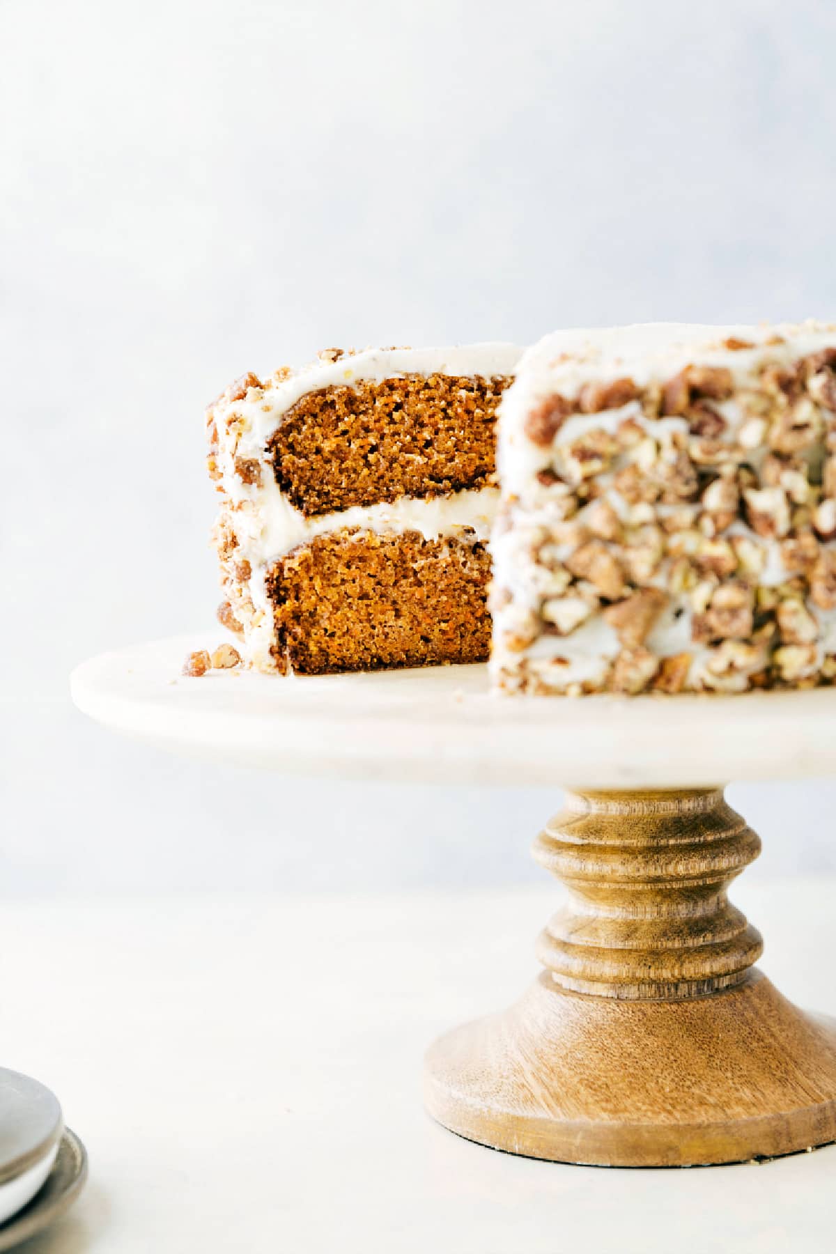 This carrot cake rests on a cake stand with a large slice removed, revealing its rich, layered interior.