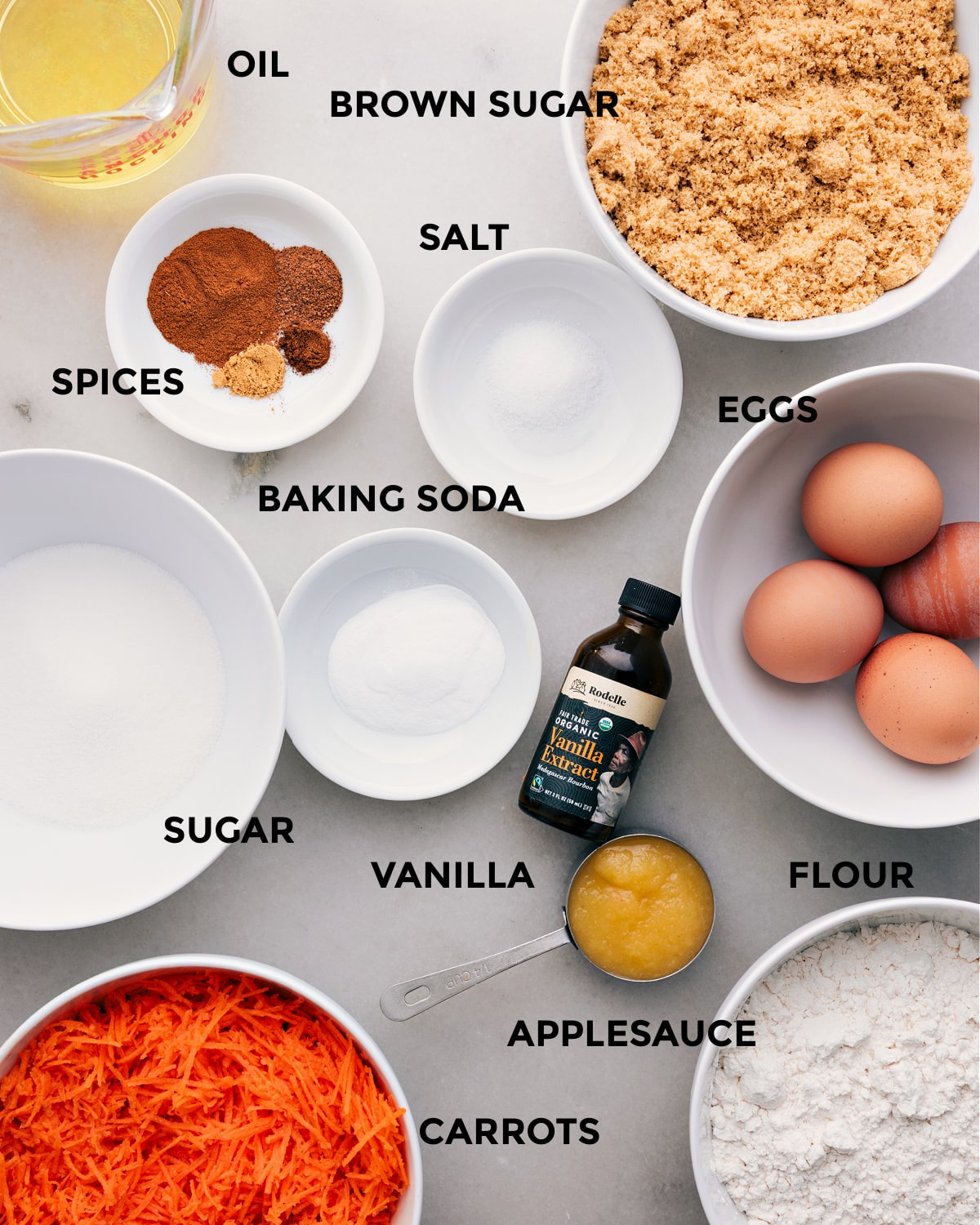 Ingredients In Carrot Cake Recipe I’ve prepped all the ingredients for easy assembly—oil, brown sugar, eggs, salt, spices, baking soda, vanilla, sugar, flour, applesauce, and carrots.