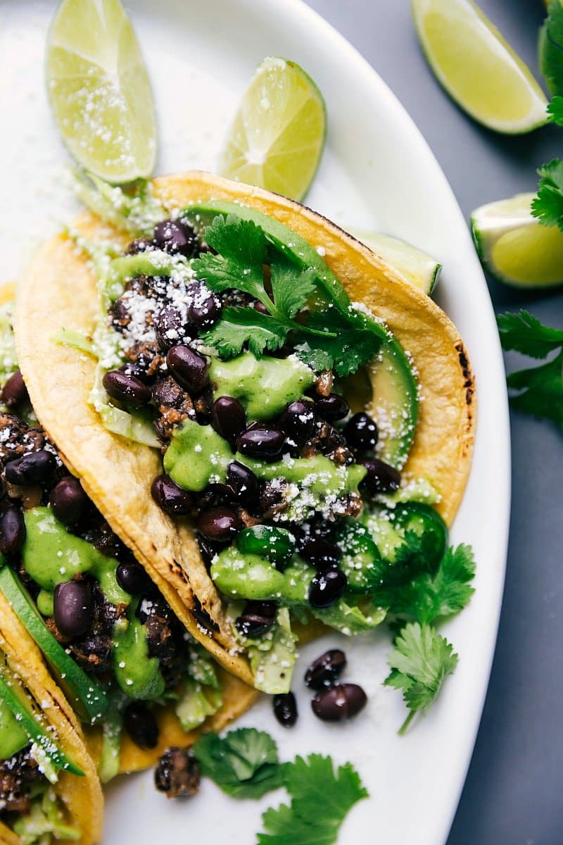 Tasty Black Bean Tacos Drizzled with Homemade Cilantro Sauce and Fresh Limes on the Side, Ready to Savor. Black bean tacos with cilantro sauce and limes, ready to eat.