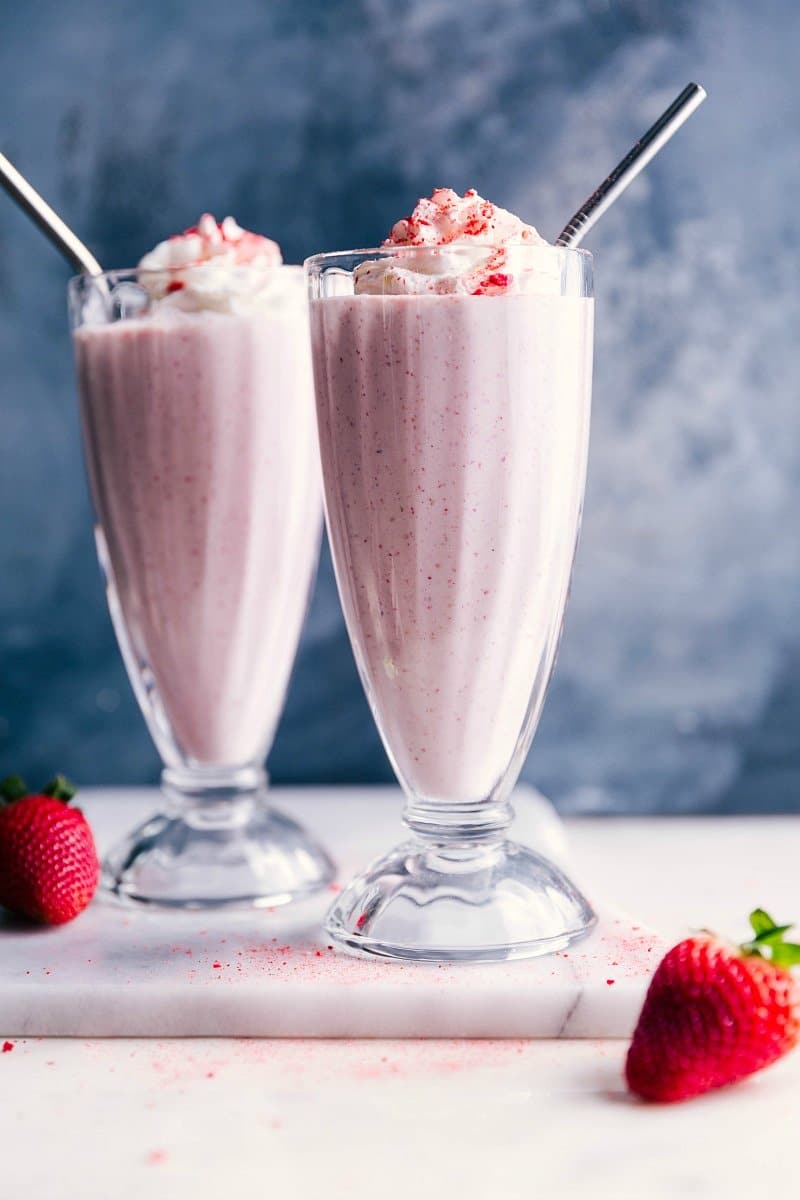 Two Strawberry Milkshakes with Whipped Cream and Straws, a Thick and Delicious Dessert Two strawberry milkshakes with whipped cream on top and straws in them, a thick and delicious dessert.