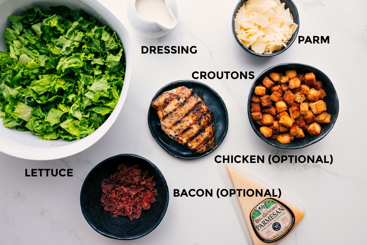 Ingredients In Caesar Salad Recipe All the ingredients prepped and ready for easy assembly: lettuce, dressing, Parmesan, croutons, bacon, and chicken.