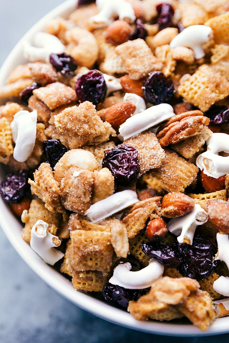 This addicting Dried Cherry Snack Mix is loaded with cereal, nuts, dried tart cherries, yogurt-covered pretzels, and covered in a cinnamon-sugar coating.ย Recipe via chelseasmessyapron #pretzels #nuts #almonds #dried #tart #cherry #sweet #snack #mix Overhead image of the snack mix in a bowl ready to be eaten