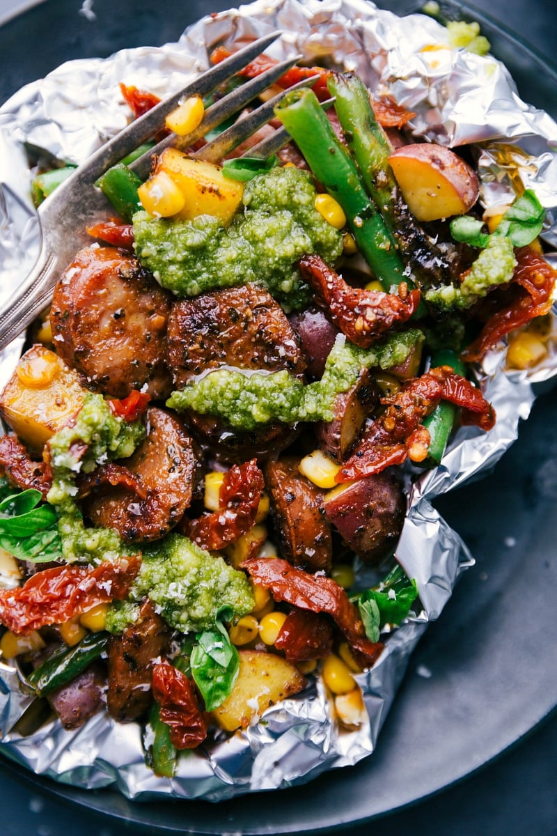 Foil Pack Feast: Fresh Pesto Topping Over Robust Ingredients Hearty foil pack dinner topped with fresh pesto, revealing its savory ingredients.