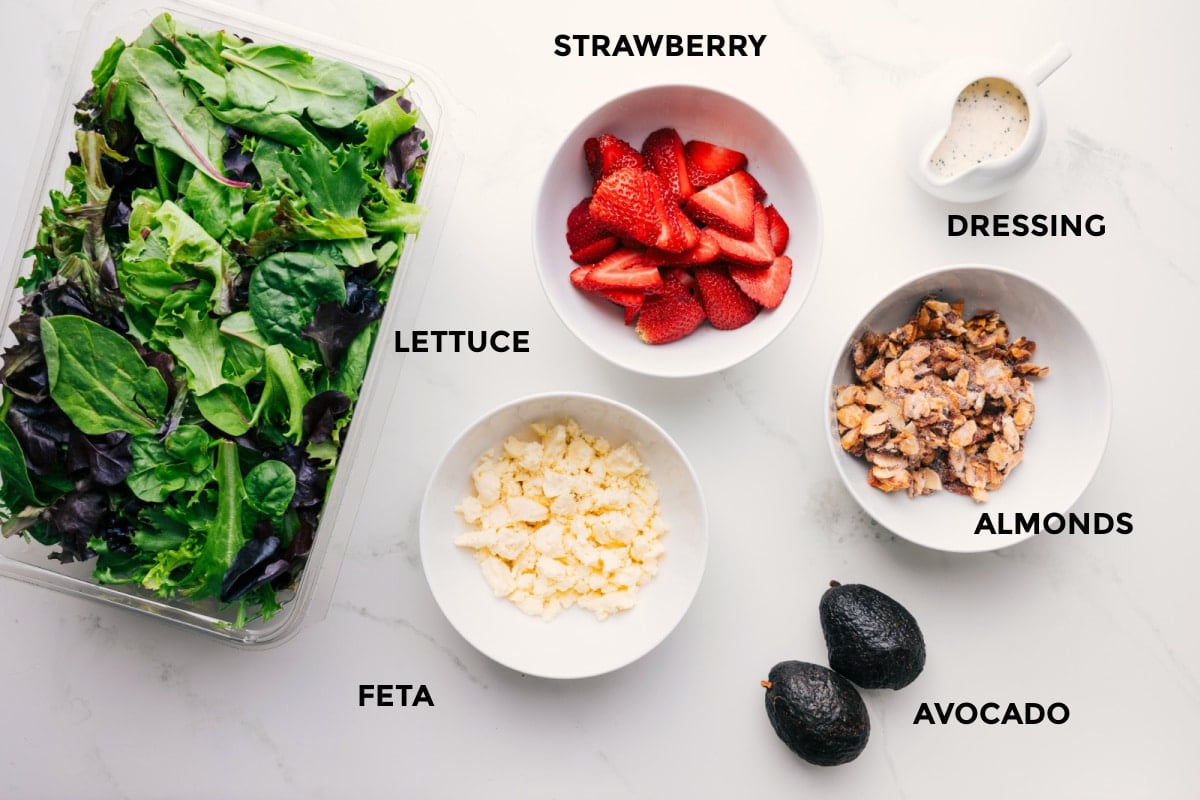 Ingredients In Strawberry Poppyseed Salad Recipe Ingredients for this recipe prepped and ready for easy assembly, including the fruit, dressing, almonds, avocado, feta, and lettuce.