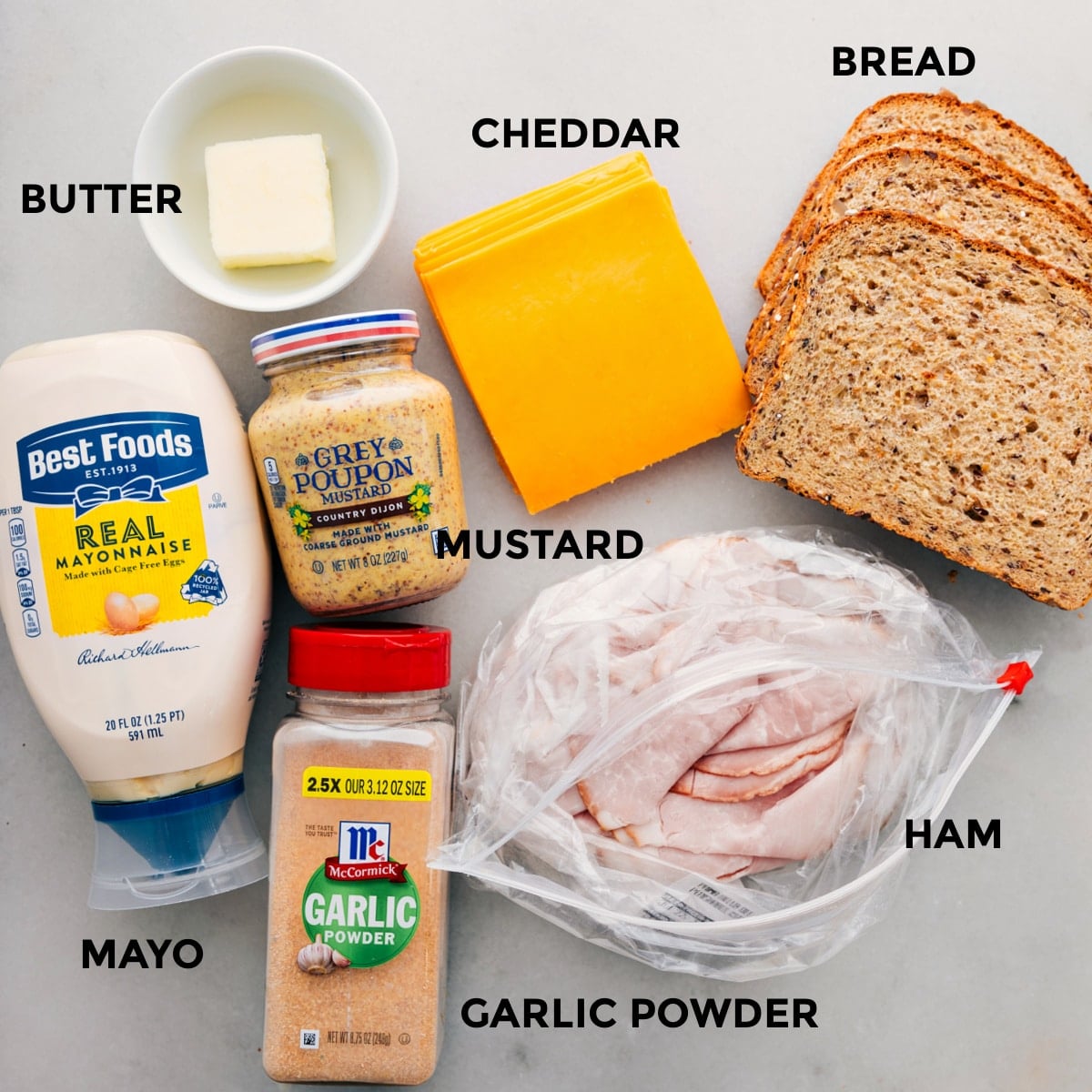 Ingredients In Ham and Cheese Sandwich All the ingredients in this recipe including the meat, bread, cheddar, mustard, butter, mayo, and garlic powder prepped out for easy assembly.