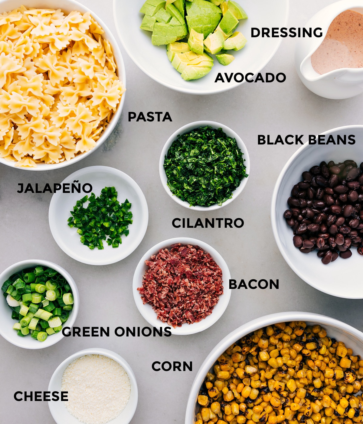 Ingredients In Mexican Street Corn Pasta Salad All the ingredients for this recipe prepped and ready for easy assembly: dressing, avocado, black beans, cilantro, noodles, bacon, green onions, corn, and cheese.