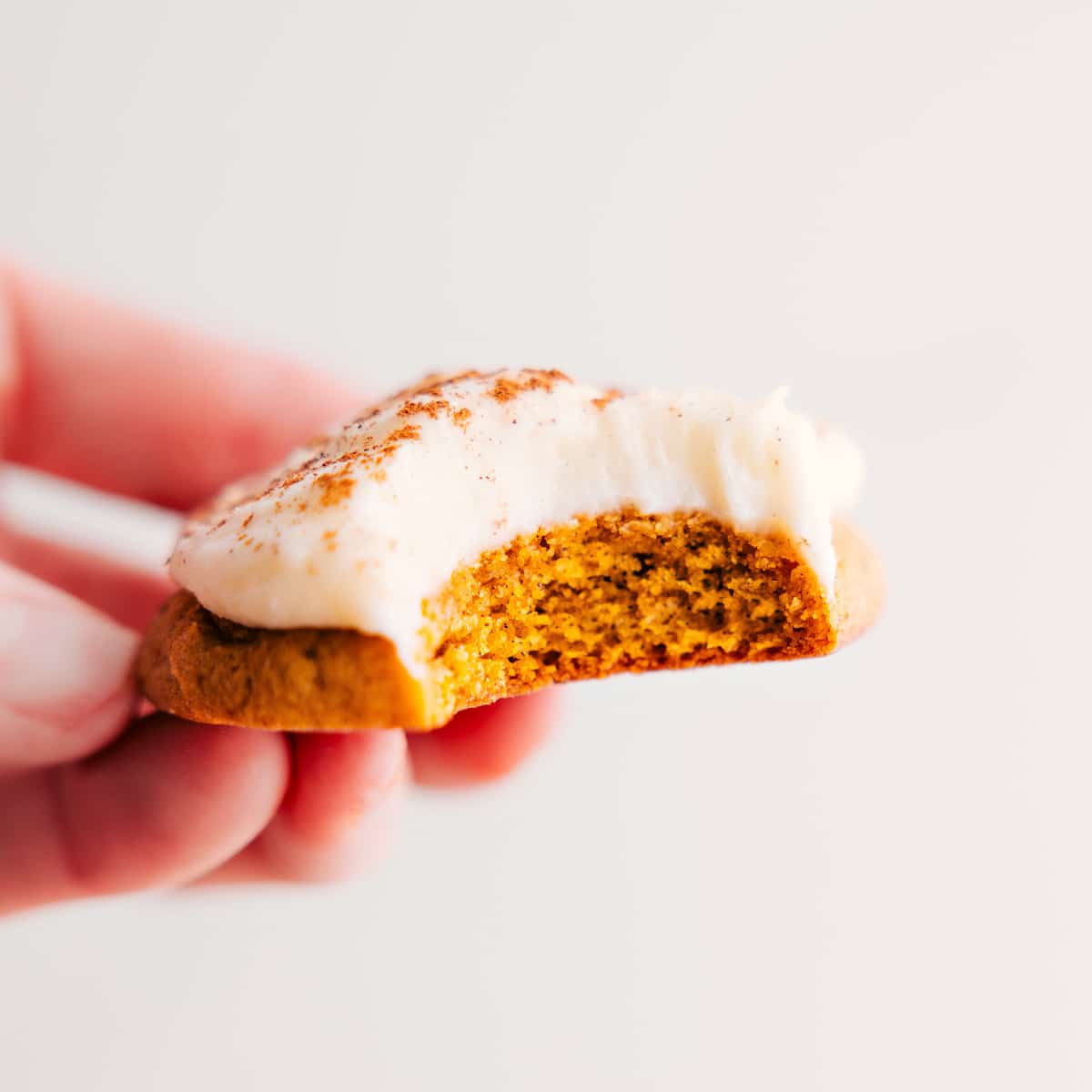Pumpkin Cookies Topped With The Best Cream Cheese Frosting A pumpkin cookie with cream cheese frosting and a bite taken out.