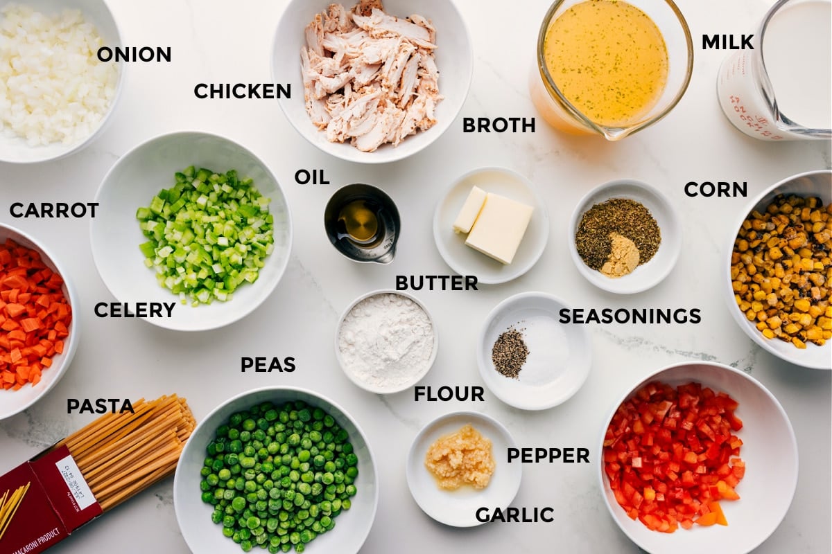 Ingredients In Creamy Chicken Noodle Soup Recipe Prepped ingredients for creamy chicken noodle soup including onion, carrot, celery, pasta, peas, chicken, oil, butter, flour, garlic, seasonings, broth, milk, corn, and peppers.