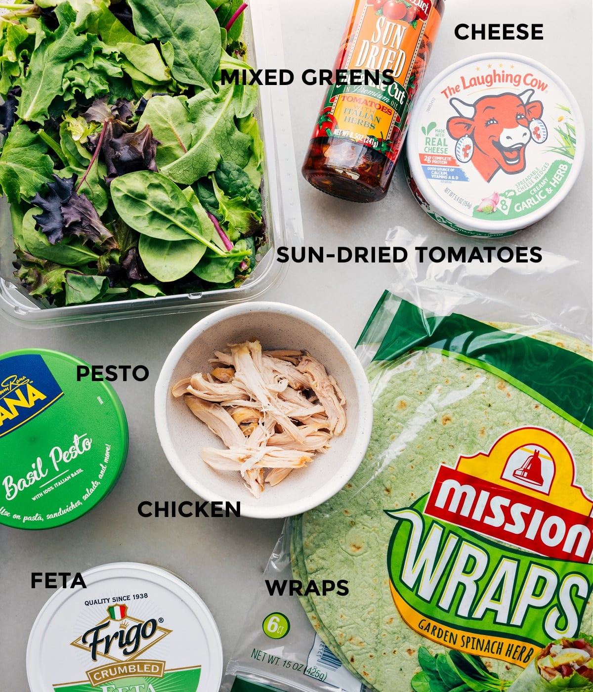 Ingredients In Mediterranean Wrap Recipe All the ingredients in this recipe prepped out for easy assembly, including pesto, chicken, mixed greens, cheese, tortillas, and feta.