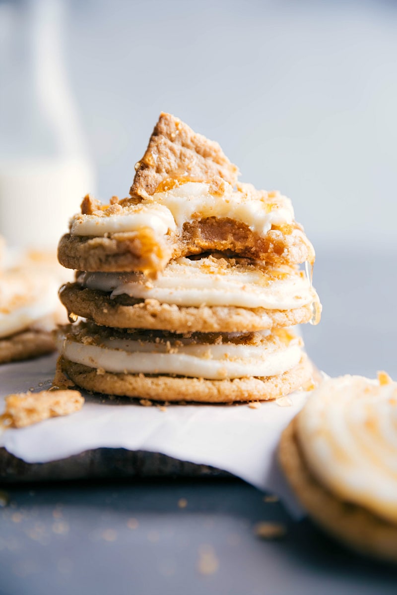 Several frosted honey graham cookies stacked up, topped with graham cracker crumbs, with a bite taken from the top cookie, revealing the soft interior.