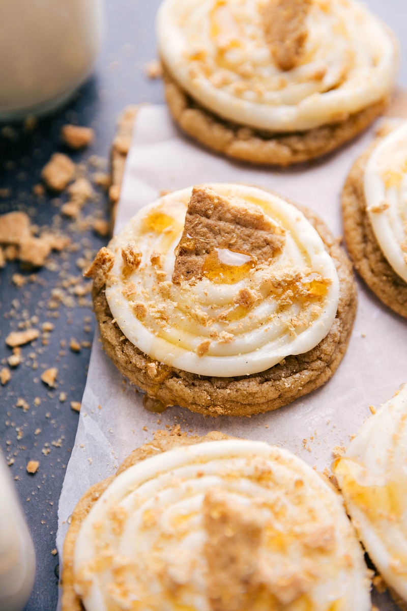 Garnished Frosted Honey Graham Cookies Frosted honey graham cookies topped with creamy frosting, garnished with graham cracker crumbs, a drizzle of honey, and a large graham cracker piece.