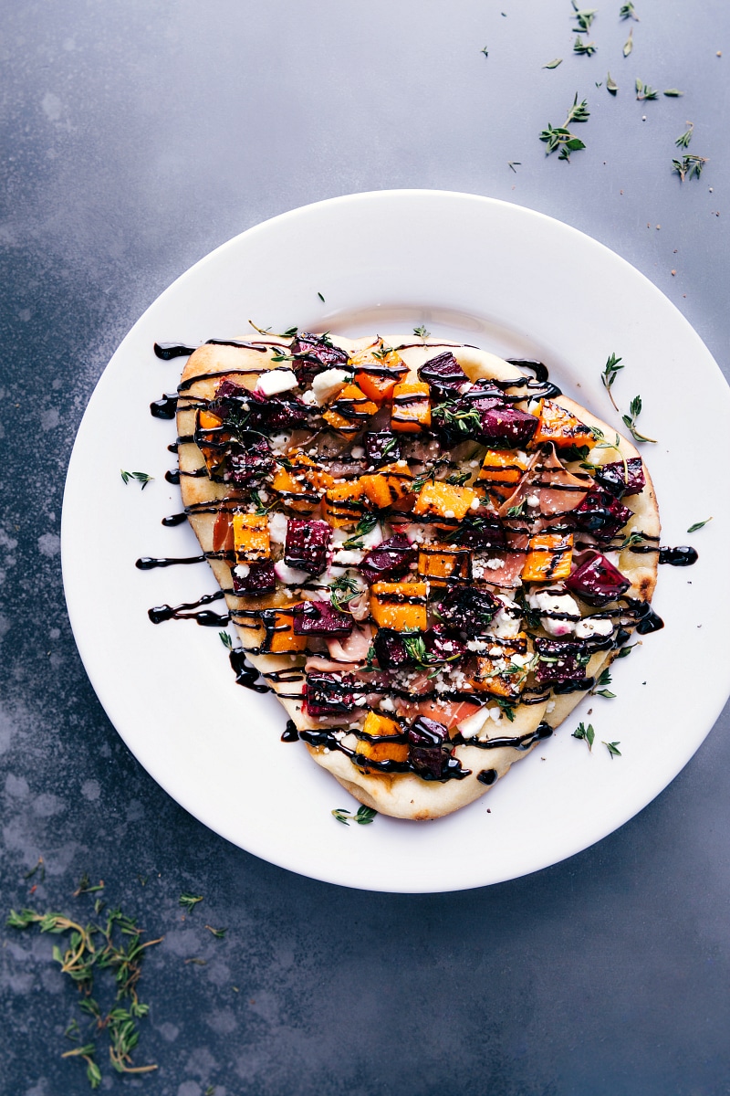 This Beet and Goat Cheese Flatbread makes for a show-stopping, flavorful holiday appetizer. These flatbreads are cooked on the grill (save that precious oven space!) and are topped with grilled butternut squash and beets! Recipe via chelseasmessyapron #pizza #healthy #quick #easy #simple #fall #grilled #dinner #butternutsquash #thyme #beet #goatcheese #flatbread Overhead image of the beet and goat cheese flatbread with a balsamic glaze over it all ready to be served