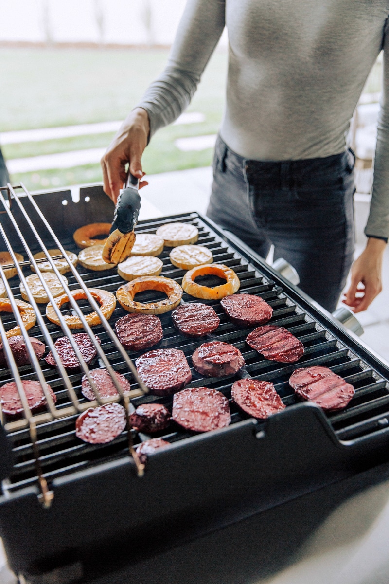 These flatbreads are cooked on the grill (save that precious oven space!) and are topped with grilled butternut squash and beets using Home Depotโs Weberยฎ E-Spirit Black grill! Recipe via chelseasmessyapron #pizza #healthy #quick #easy #simple #fall #grilled #dinner #butternutsquash #thyme #beet #goatcheese #flatbread Side angle of Chelsea flipping the butternut squash on the grill for this beet and goat cheese flatbread