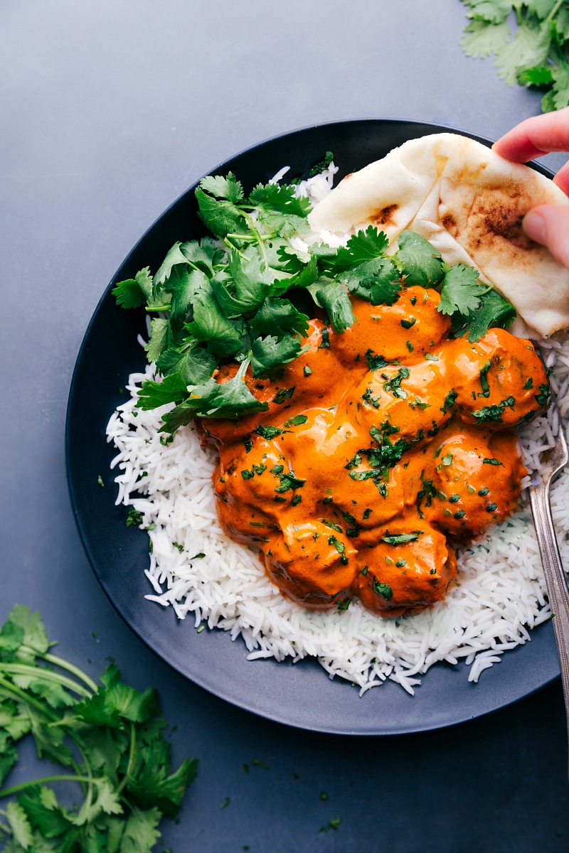 Butter Chicken Meatballs with Rice and Naan Plate with butter chicken meatballs served on a bed of rice, garnished with fresh cilantro, with naan bread on the side.