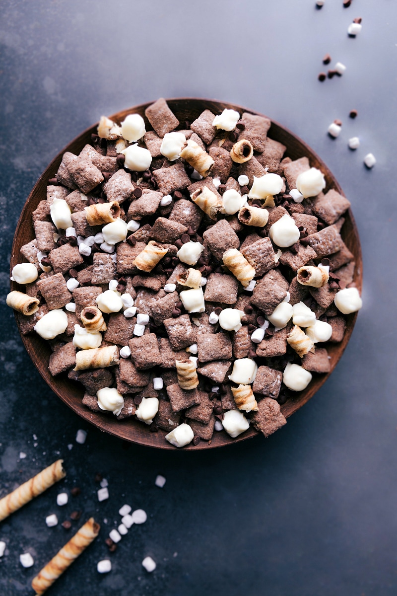 Hot Chocolate Snack Mix is inspired by our favorite chilly weather beverage -- hot chocolate! Chocolate Chex® cereal is coated in melted chocolate and tossed with a hot cocoa powdered sugar blend. Add in some white chocolate-covered marshmallows and chocolate chips for an unforgettable snack mix! Recipe via ChelseasMessyApron #marshmallows #cozy #christmas #holidays #minimarshmallows #hotchocolate #snack #mix Image of a bowl full of Hot Chocolate Snack Mix.