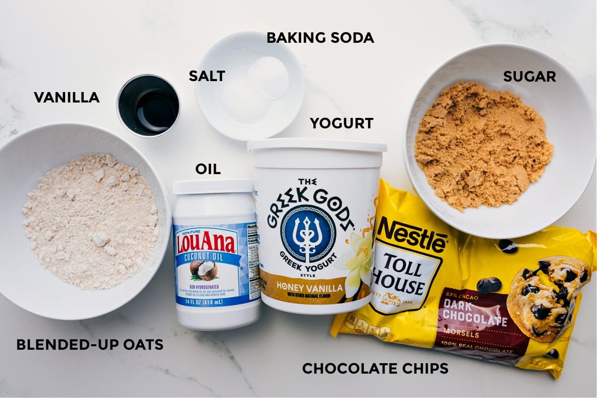 Ingredients In Healthy Brownies Ingredients prepped for easy assembly: blended oats, vanilla, salt, baking soda, oil, yogurt, chocolate chips, and sugar.