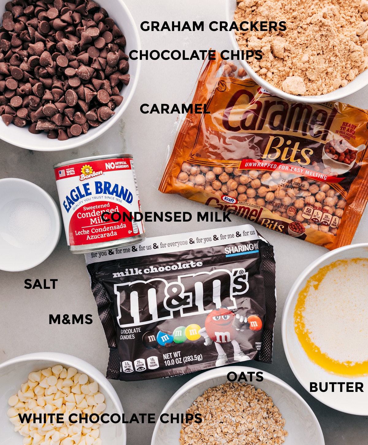 Ingredients In Magic Cookie Bars All the ingredients are prepped and ready for easy assemblyโgraham crackers, caramel bits, condensed milk, chocolate chips, M&Ms, butter, oats, and salt.