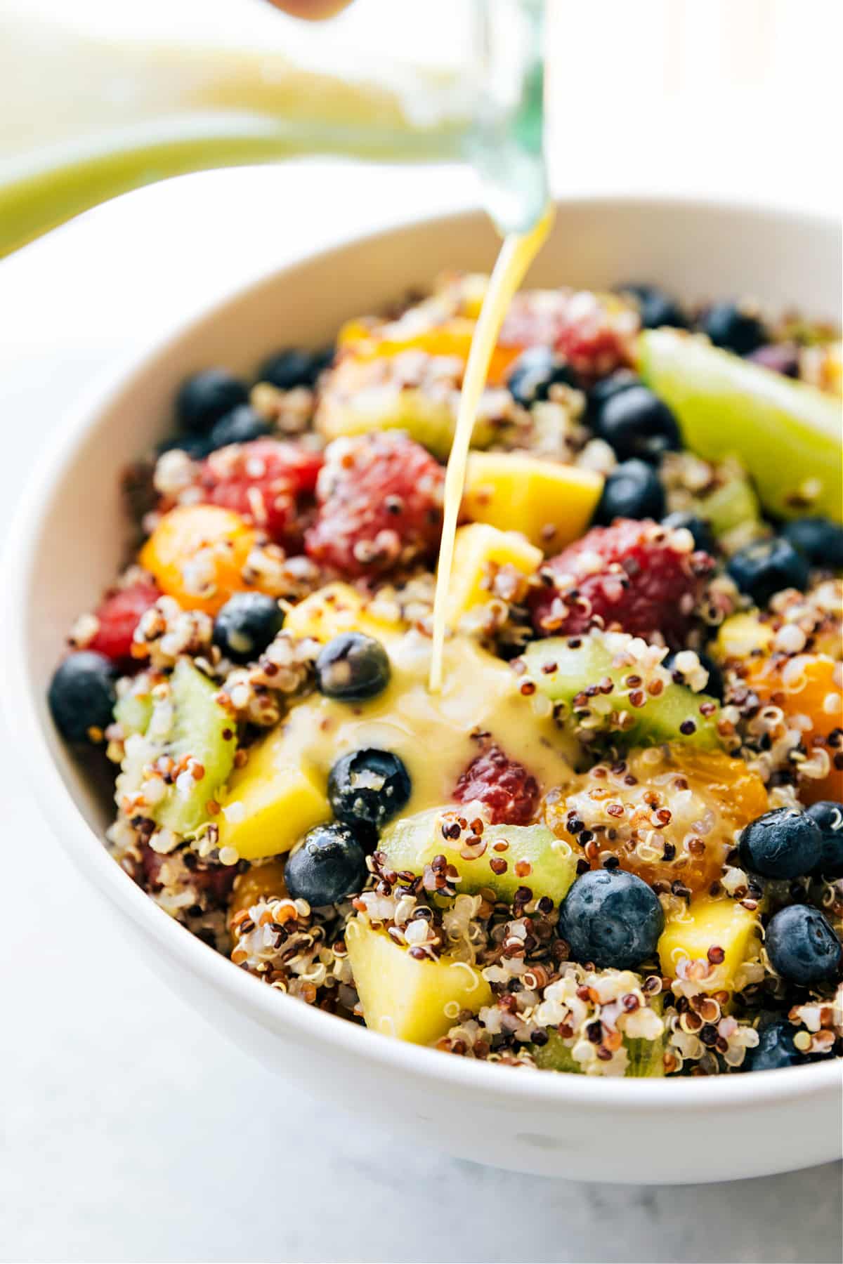 Our Favorite Quinoa Fruit Salad Quinoa Fruit Salad with the dressing being poured over it.
