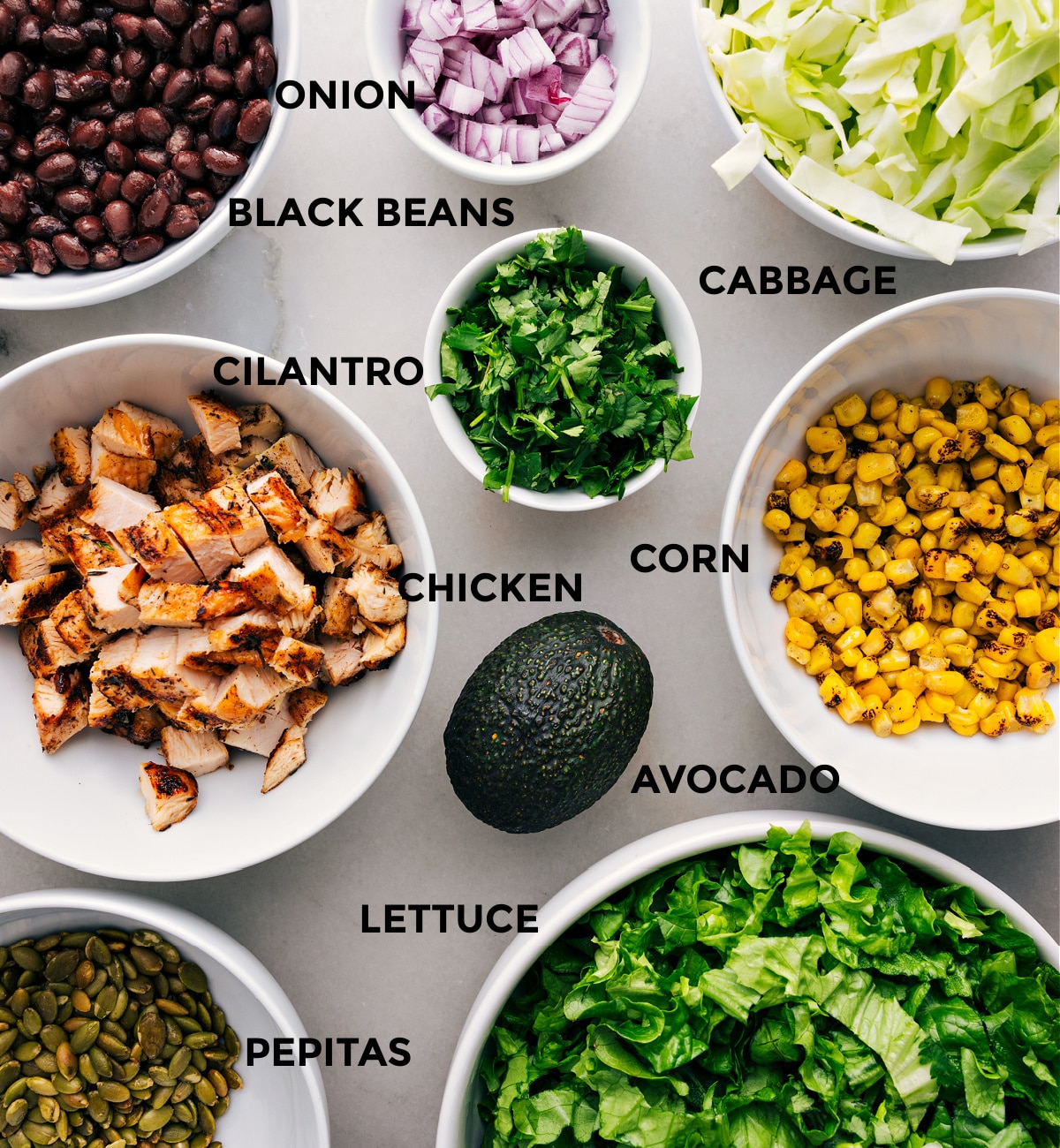 Ingredients In Chipotle Chicken Salad Lettuce and cabbage, pepitas, corn, black beans, avocado, chicken, cilantro, and red onion prepped out for easy assembly of this recipe.