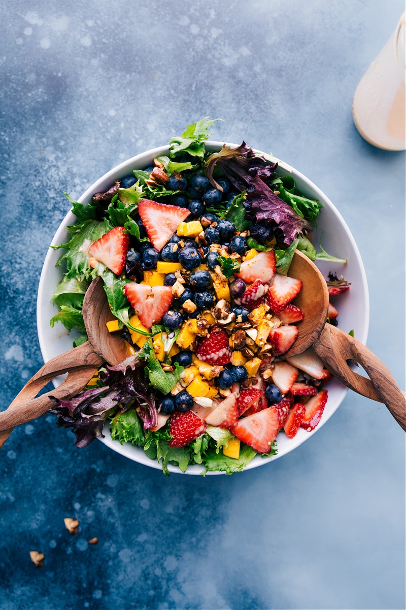This vibrant, fresh, and lively Mango Salad is loaded with fresh fruit, cinnamon almonds, and dressed with a cinnamon-yogurt dressing. Be prepared for a salad addiction! Recipe via ChelseasMessyApron.com #mangosalad #mango #berries #fruity #salad #cinnamonalmonds #almonds #cinnamon #yogurtdressing Overhead view of Mango Salad, ready to serve.